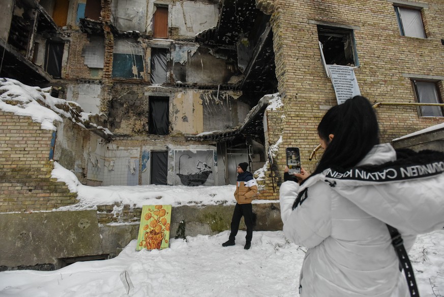 epa10347162 People take pictures near a damaged apartment block with a mural by street artist Banksy, depicting a man in a bathtub scrubbing his back with a brush (rear), in Horenka, near Kyiv, Ukrain ...