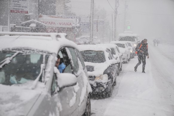 Vehicles drive as a man cross a street during snowfall in Agios Steganos, north of Athens, on Monday, Jan. 24, 2022.The wave of bad weather hitting Greece is forecast to continue through Tuesday, and  ...