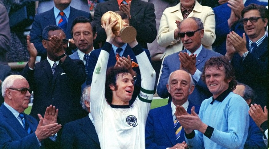 Surrounded by applauding spectators, Franz Beckenbauer, center, team captain of the winning German national soccer team at the 1974 world soccer championship presents the trophy in Munich&#039;s, Germ ...