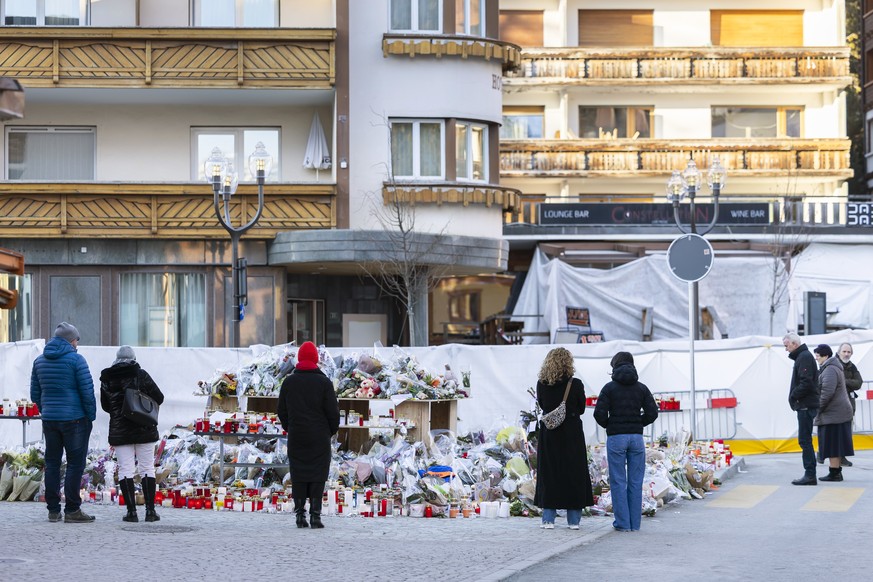 epa12628948 Flowers and candles are pictured in tribute to the victims after the fire at the 'Le Constellation' bar and lounge in Crans-Montana, Switzerland, 05 January 2026. At least 40 peo ...