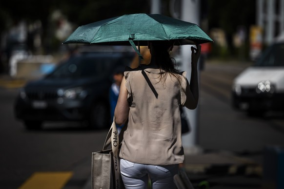 A woman protects herself from the sun with an umbrella while walking along a street as a heat wave reaches the country in Zurich, Switzerland, on Monday, July 29, 2024. (KEYSTONE/Michael Buholzer)
