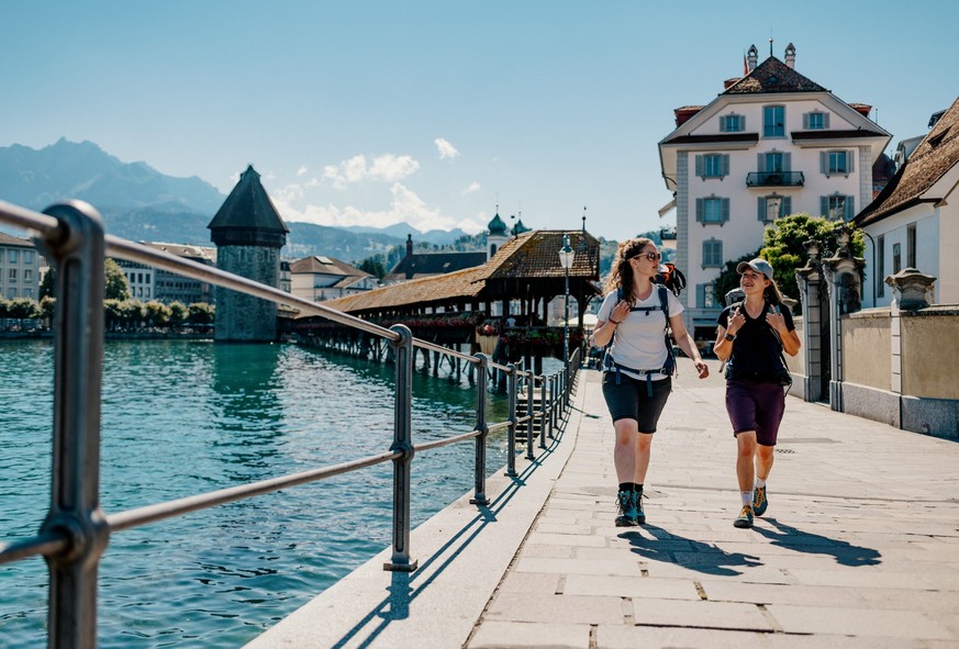 Zwei Wanderinnen spazieren durch die Altstadt der Stadt Luzern mit der Kapellbrücke und dem Wasserturm im Hintergrund