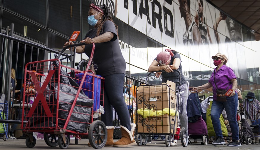 Pedestrians wait in line to collect fresh produce and shelf-stable pantry items outside Barclays Center as Food Bank For New York City provides assistance to those in need due to the COVID-19 pandemic ...