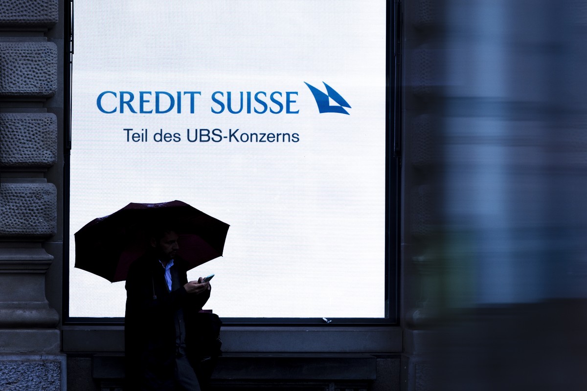 epa11386769 A person holding an umbrella is silhouetted against a screen of Swiss bank Credit Suisse with the words 'Part of the UBS Group', at Zurich's Paradeplatz in Zurich, Switzerla ...