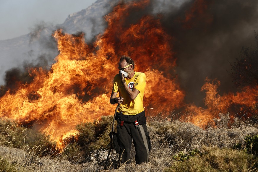 epa06119065 A volunteer firefighter covers his face while trying to extinguish flames during a bushfire in Anavyssos near Athens, Greece, 31 July 2017. A large fire that broke out in a forested area i ...