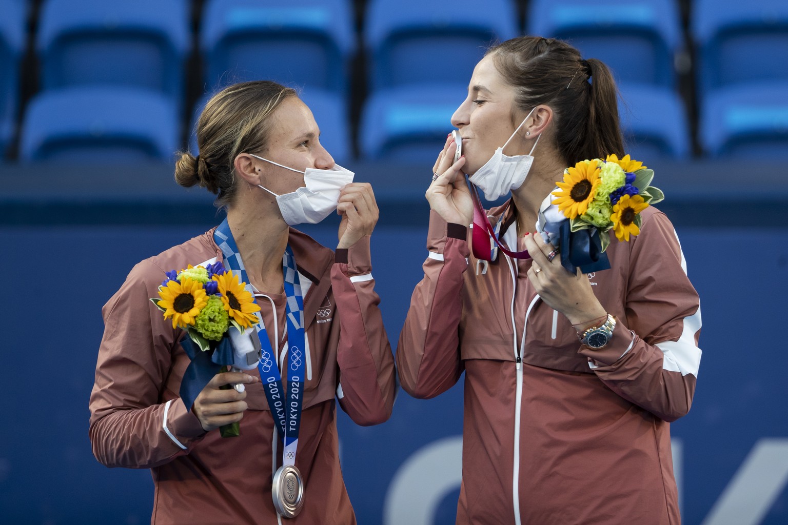 Switzerland&#039;s Belinda Bencic, right, kisses her silver medal next to teammate Viktorija Golubic on the podium after the women&#039;s tennis doubles gold medal match against Barbora Krejcikova and ...