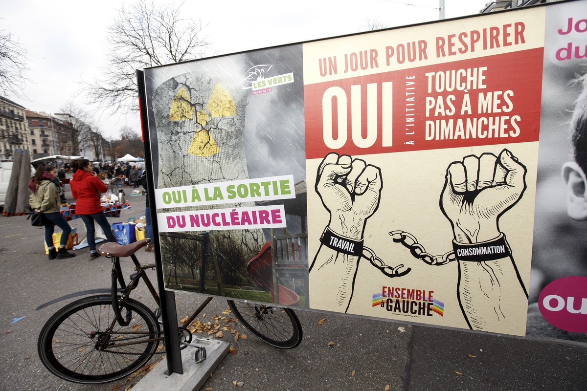 Des personnes passent vers une affiche pour la votation federale sur l'initiative "Sortir du nucleaire" et d'une affiche pour la votation cantonale genevoise "Touche pas a mes ...