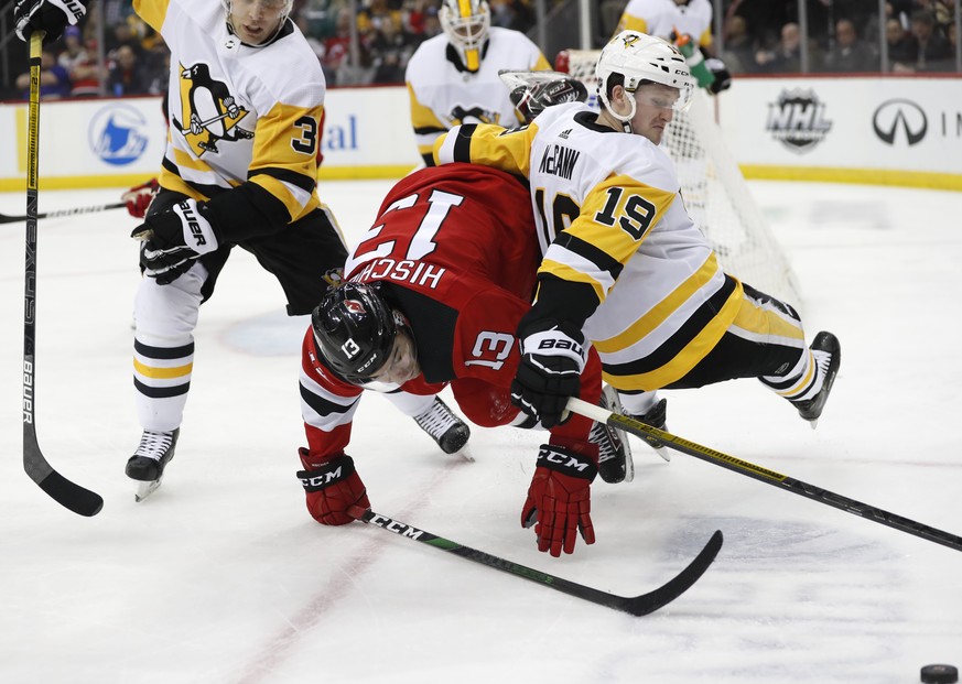 Pittsburgh Penguins center Jared McCann (19) falls over New Jersey Devils center Nico Hischier (13) as they try to get to the puck, lower right, with Penguins defenseman Jack Johnson (3) watching duri ...