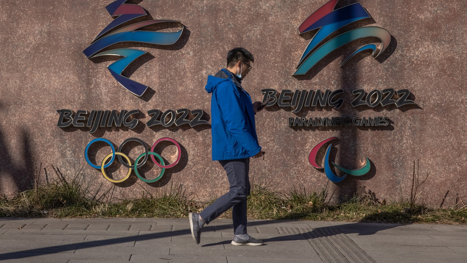 epa09614040 A man walks past the 2022 Beijing Winter Olympic and Paralympic emblems next to the headquarters of the 2022 Beijing Winter Olympics organising committee, at the Shougang Industrial Park,  ...