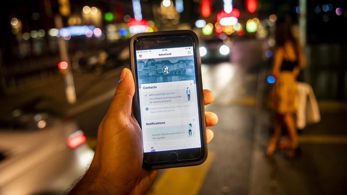 Une personne regarde sur son smartphone l'application SwissCovid alors que des personnes font la fete lors d'une soiree d'ete le samedi 27 juin 2020 dans le quartier du Flon a Lausanne. ...