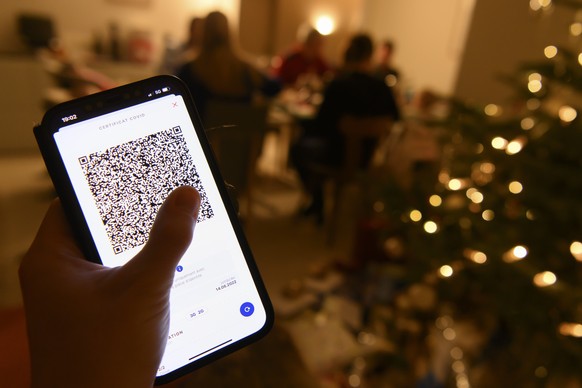 Eine Person haelt ein Smartphone mit Covid-Zertifikat bei einem Weihnachtsessen an Heiligabend mit der Familie, am Freitag, 24. Dezember 2021, in Duedingen. (KEYSTONE/Anthony Anex)