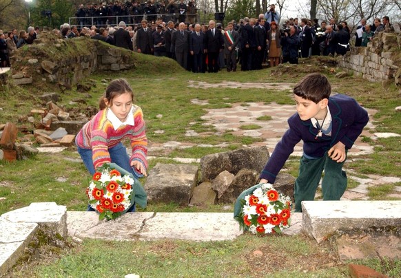 A photo of a young girl and a young boy, one from Italy and one from Germany, laying flowers on the remains of the steps of the altar of the church of San Martino - where Nazi troops burst in and shot the priest before herding dozens of women and children into the cemetery and killing them, Wednesday, 17 April 2002 as on the background German president Johannes Rau, Marzabotto mayor Andrea De Maria (with tricolour ribbon) and Italian president Carlo Azeglio Ciampi, pay homage to the victims of the 
