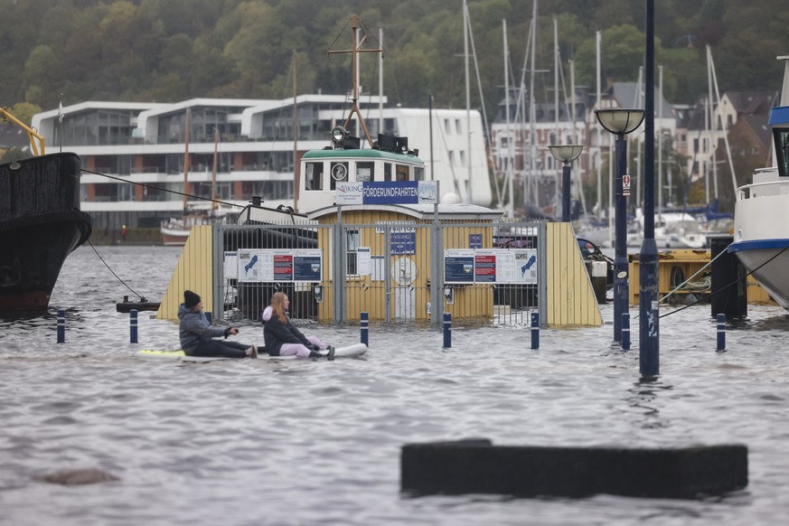 October 20, 2023, Schleswig-Holstein, Flensburg: Two people paddle across the water near the harbor on a stand-up paddleboard.  A powerful storm pushes the waters of the Baltic Sea onto land, causing flooding...