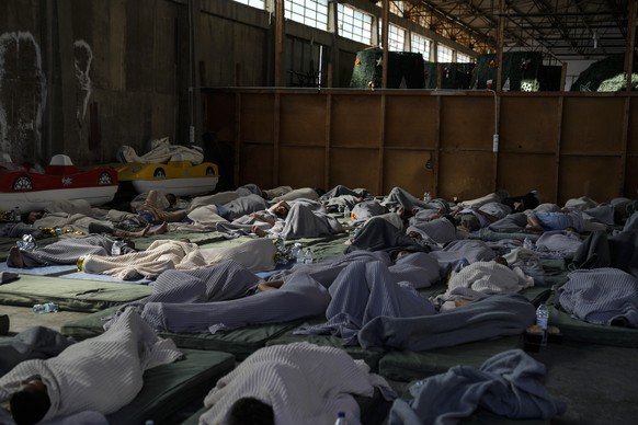Survivors of a shipwreck sleep in a warehouse in the harbor in the town of Kalamada, about 240 kilometers (150 miles) southwest of Athens, Wednesday, June 14, 2023.  A fishing boat carrying migrants capsized...