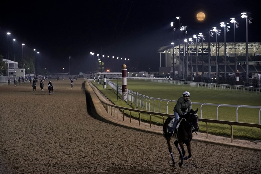 Horses work out at Churchill Downs as the moon sets in the distance Friday, May 5, 2023, in Louisville, Ky. The 149th running of the Kentucky Derby is scheduled for Saturday, May 6. (AP Photo/Charlie  ...