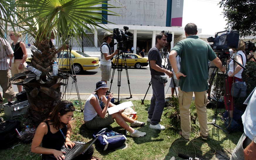 Reporters wait outside the Hilton hotel of Athens to cover the arrival of two Greek athletes, August 13, 2004. Greek Olympic sprinters Costas Kenteris and Katerina Thanou, who had been summoned to app ...