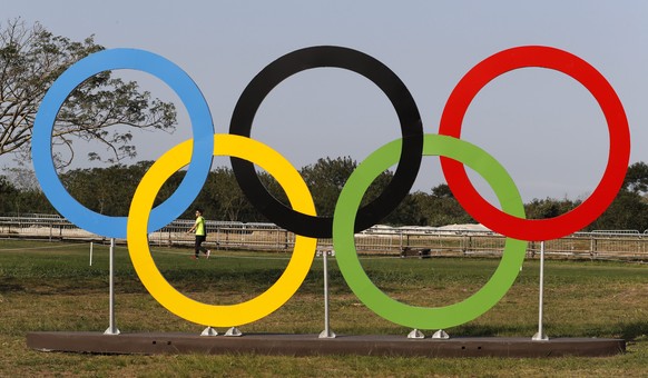 epa05455621 An unidentified member of an Olympic equestrian team walks the cross country course of the the eventing competition and passes Olympic rings in the grounds of the Olympic Equestrian Center ...