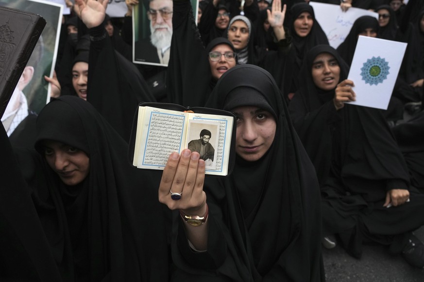 A demonstrator holds up a copy of the Quran and a portrait of the Supreme Leader Ayatollah Ali Khamenei in a protest against Sweden in front of the Swedish Embassy in Tehran, Iran, Friday, July 21, 20 ...