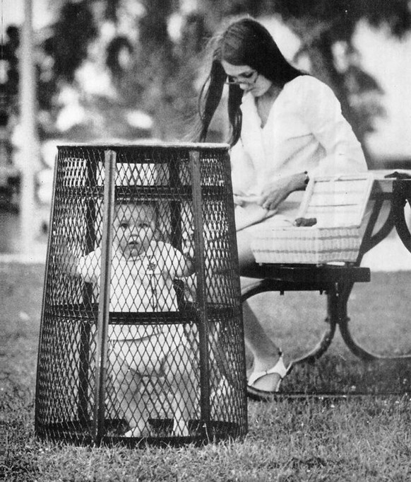 Mama benutzt einen Mülleimer, um ihr Baby zu halten, während sie 1969 im Park häkelt.