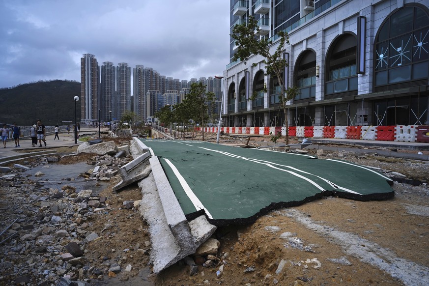 People walk past debris caused by Typhoon Mangkhut outside a housing estate on the waterfront in Hong Kong, Monday, Sept. 17, 2018. Hong Kong and southern China hunkered down as strong winds and heavy ...