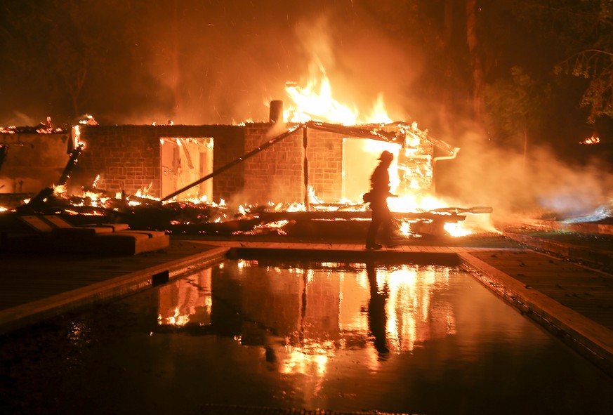 A firefighter walks by the a burning home in Malibu, Calif., Friday, Nov. 9, 2018. A Southern California wildfire continues to burn homes as it runs toward the sea. Winds are blamed for pushing the fi ...