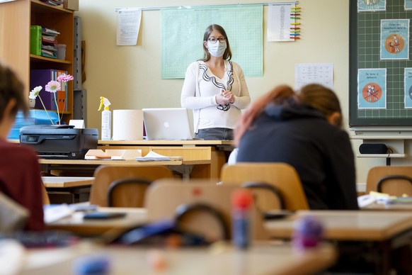 A teacher wearing protective face mask as she teaches close to pupils at a primary school in Morges, Switzerland, Monday, May 11, 2020. Swiss primary and secondary schools reopened with half of the st ...