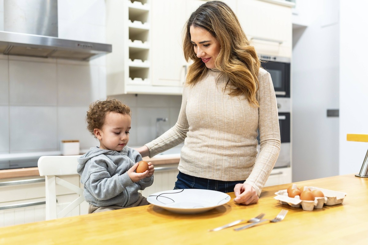 Glückliche Mutter und neugieriger Junge treffen sich in der Küche, bereiten frische Eier für eine gesunde Mahlzeit zu und lernen zu Hause gemeinsam über Kochen und Ernährung Happy mother and curious t ...