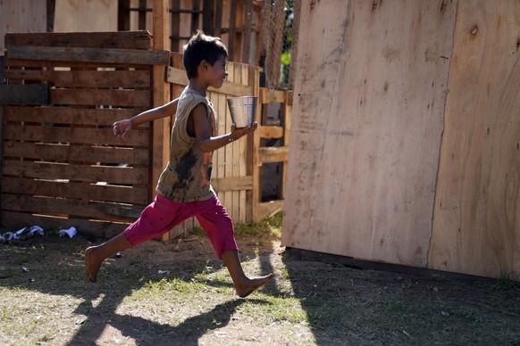 A child, who was displaced from his home by the rising waters of the Paraguay River, runs past carrying a container filled with water, on the grounds of his temporary shelter, in Asuncion, Paraguay, S ...