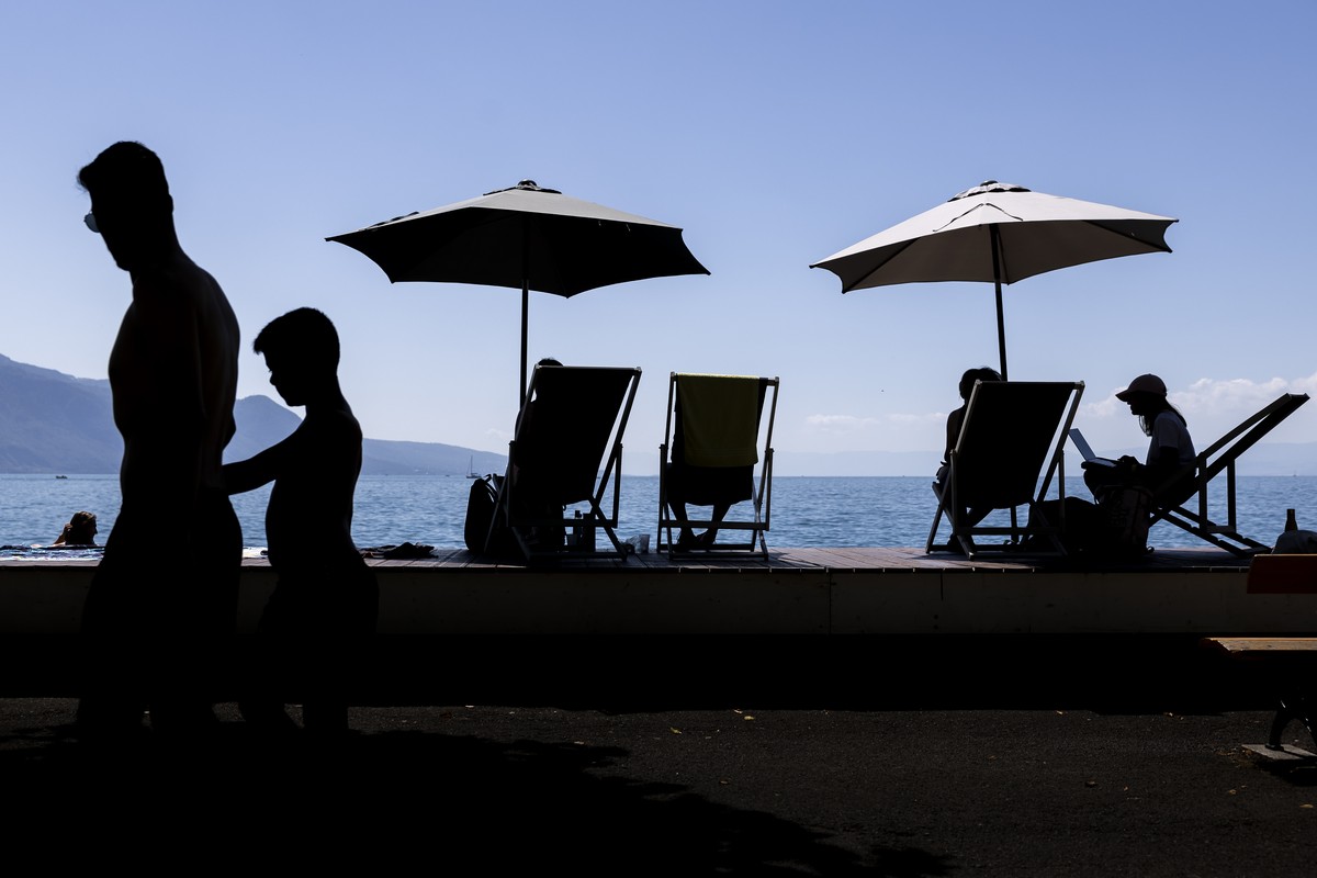 People take a break under an umbrella and enjoy the warm summer weather on the shores of Lake Geneva in front of the Swiss Alps mountains, in Vevey, Switzerland, Saturday, July 8, 2023 (KEYSTONE/Cyril ...
