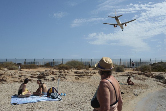 Sunbathers enjoy the beach as an airplane lands on the Balearic Islands capital of Palma de Mallorca, Spain, Wednesday, July 29, 2020. Concerns over a new wave of coronavirus infections brought on by  ...