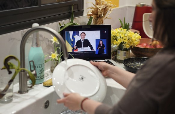 A woman washes dishes while watching French President Emmanuel Macron making a television address on the situation in Ukraine, Wednesday, March 2, 2022, in Lyon, central France. (AP Photo/Laurent Cipr ...