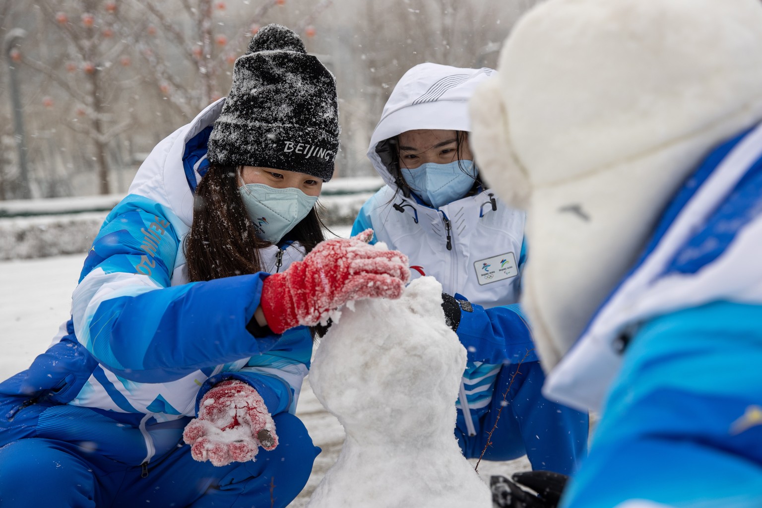 epa09751653 Olympic staff build a snow man during a snow fall in a park part of the Olympic bubble near the Main Media Centre during the Beijing 2022 Olympic Games, Beijing, China, 13 February 2022. E ...