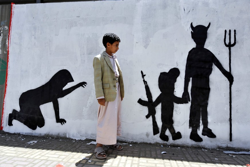 epa04161922 A Yemeni boy looks at graffiti sprayed on a wall depicting a child soldier walking with evil during a campaign to end the recruitment and use of children in conflicts, in Sana’a, Yemen, 10 ...