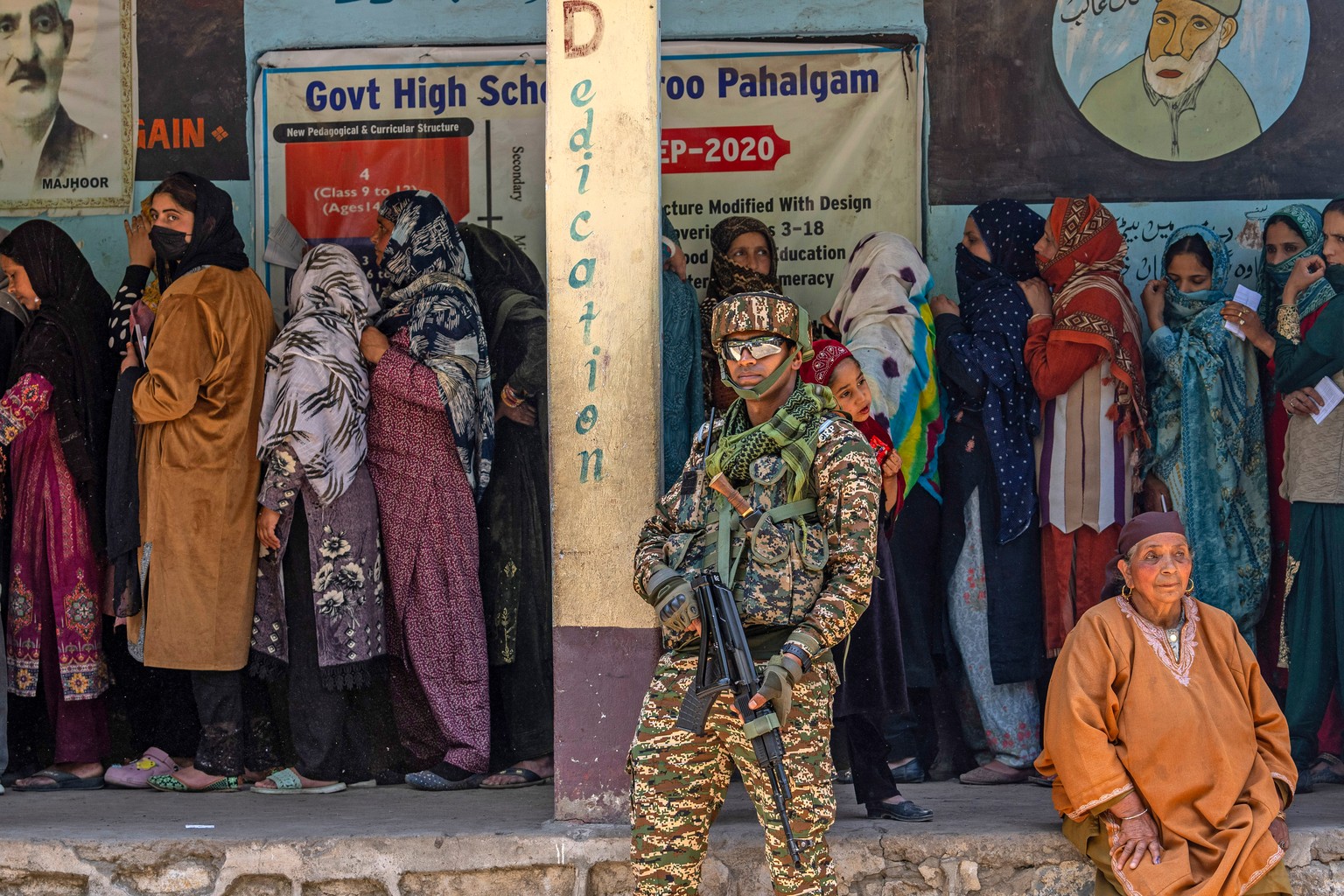 A paramilitary soldier stands guard as Kashmiri women queue up at a polling booth to cast their vote in the sixth round of polling in India's national election in Lidroo, south of Srinagar, India ...