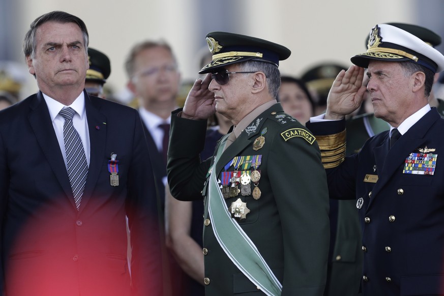 The the red kepi of military cadet in the foreground, Brazils President Jair Bolsonaro, left, receives military honors from Army Commander General Edson Leal Pujol, center, during a military ceremony  ...