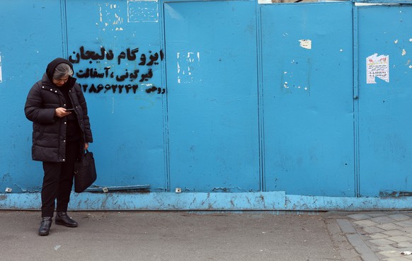 epa12660996 An Iranian woman checks her phone on a street in Tehran, Iran, 19 January 2026. Iran is experiencing a nationwide internet blackout that began on 08 January 2026, amid an intensifying wave ...