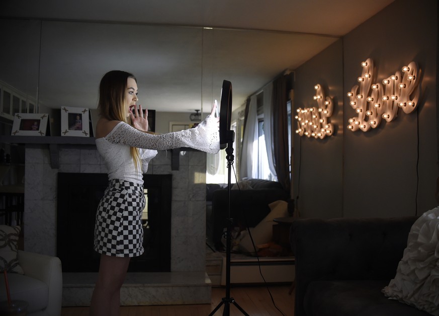 In this Feb. 28, 2018 photo, Matty Nev Luby holds up her phone in front of a ring light she uses to lip-sync with the smartphone app Musical.ly, in Wethersfield, Conn. Teens and young adults say cyber ...