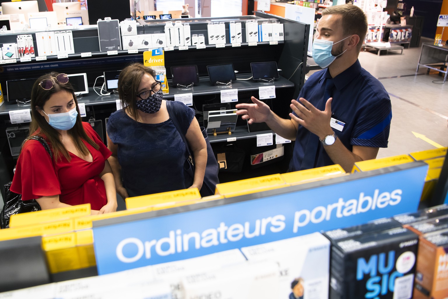 Un vendeur avec un masque sur le visage conseil des clientes dans un magasin Melectronics de la Migros le mercredi 8 juillet 2020 a Crissier. Les masques sont obligatoires dans les magasins des 10 per ...