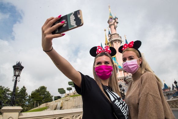 epa08547272 Visitors wearing protective face masks take a selfie picture in front of the Sleeping Beauty Castle for the official reopening of the Disneyland Paris theme park in Marne-la-Vallee, near P ...