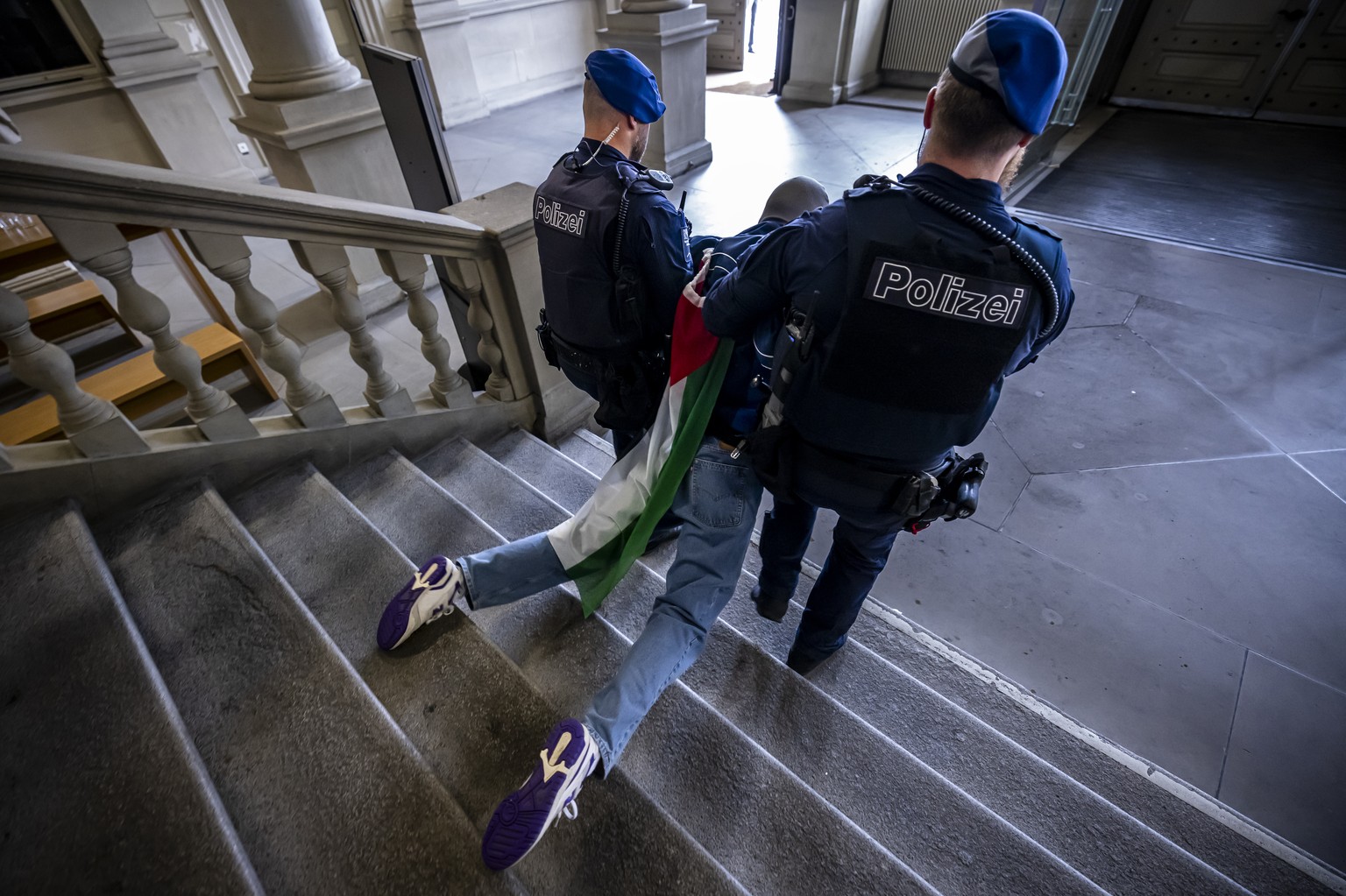 Police officers carry away a Pro-Palestinian demonstrator wearing a Palestinian flag during protest in the entrance hall of the main building of the ETH Zurich on Tuesday, May 7, 2024 in Zurich, Switz ...