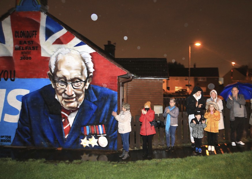 Local residents join a national clap beside a mural of Captain Sir Tom Moore in East Belfast, Northern Ireland, Wednesday, Feb. 3, 2021. Captain Moore passed away Tuesday after being treated with Covi ...
