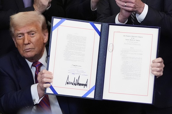 President Donald Trump holds up the GENIUS Act, a bill that regulates stablecoins, a type of cryptocurrency, after he signs the bill in the East Room of the White House, Friday, July 18, 2025, in Wash ...