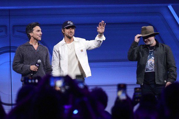 Actor Ryan Gosling, center, flanked by film directors Shawn Levy, left, and Dave Filoni waves at audience members during a fan convention called the Star Wars Celebration in Chiba, near Tokyo, Friday, ...