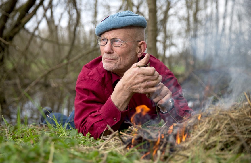 ARCHIV - 23.04.2015, Schleswig-Holstein, Rausdorf: Der deutsche Survival-Experte und Aktivist für Menschenrechte, Rüdiger Nehberg, liegt in einem Wald auf seinem Privatgrundstück neben einem selbst en ...