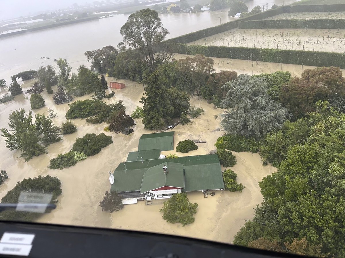In this image released by the New Zealand Defense Force on Wednesday, Feb. 15, 2023, people stand on a rooftop of a home waiting to be winched to safety by helicopter in the Esk Valley, near Napier, N ...
