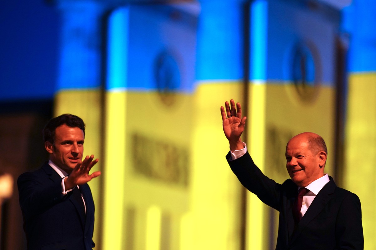 epa09936749 German Chancellor Olaf Scholz (R) and French President Emmanuel Macron (L) wave as they leave after posing for media in front of the Brandenburg Gate, illuminated in the national colors of ...