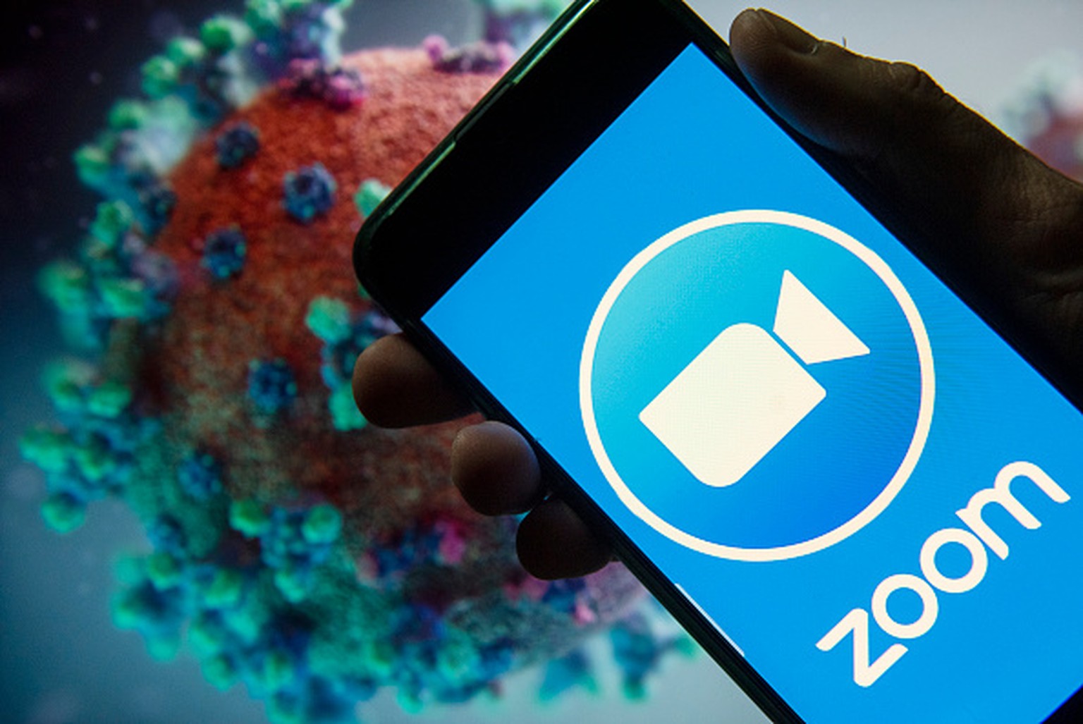 CHINA - 2020/03/22: In this photo illustration the American video Communications company Zoom logo seen displayed on a smartphone with a computer model of the COVID-19 coronavirus on the background. ( ...