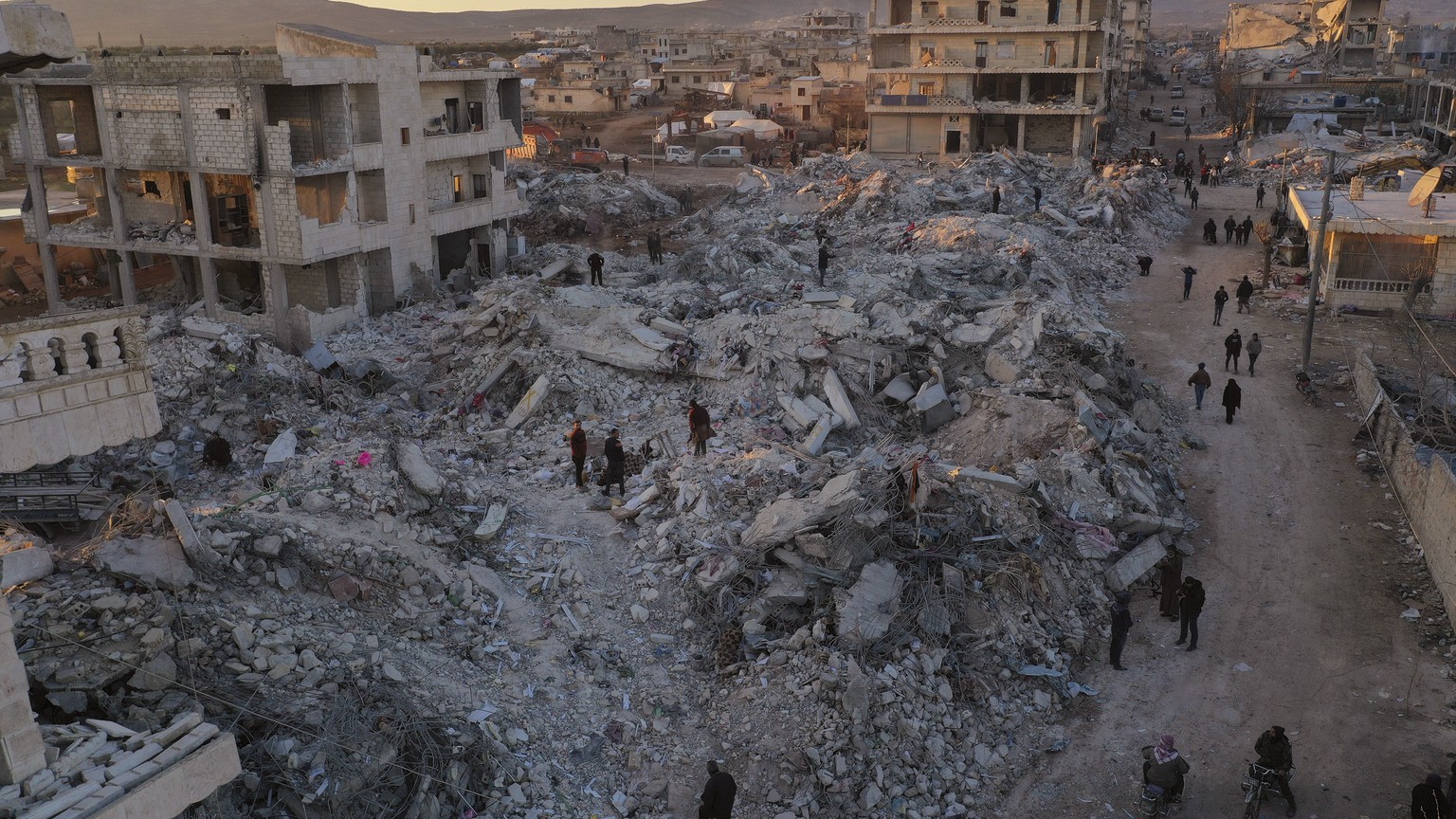 People walk past collapsed buildings following a devastating earthquake in the town of Jinderis, Aleppo province, Syria, Thursday, Feb. 9, 2023. The quake that razed thousands of buildings was one of  ...