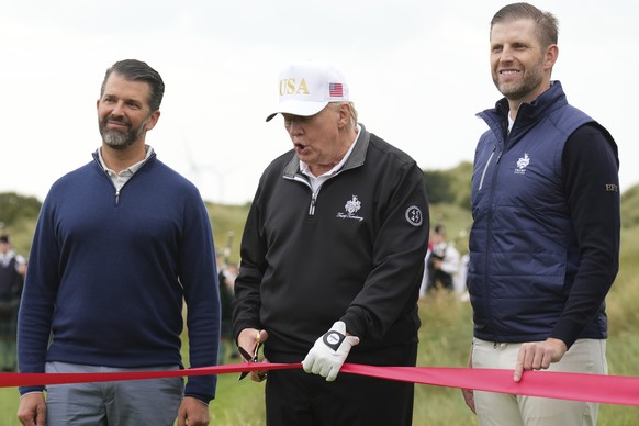 President Donald Trump cuts the ribbon, standing between Donald Trump Jr., left, and Eric Trump, during an opening ceremony for the Trump International Golf Links golf course, near Aberdeen, Scotland, ...