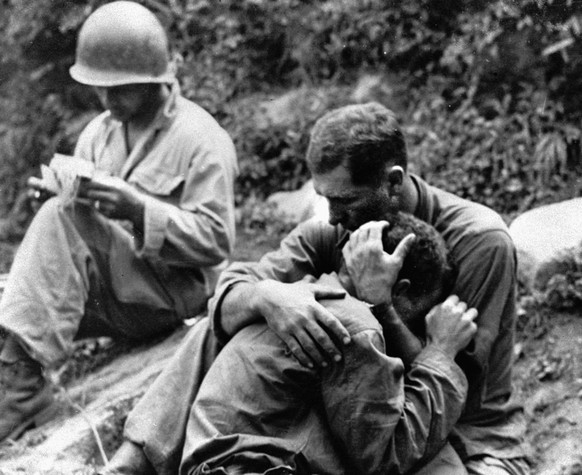 An American infantryman, his buddy killed in action in the Korean War, weeps on the shoulder of another GI somewhere in Korea, August 28, 1950. Meanwhile, a corpsman, left, goes about the business of  ...